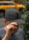 A man in NYC wearing a black baseball cap with a black UJA flame logo engraved.