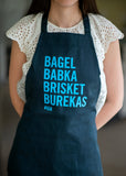 Woman wearing a black apron that says "Bagel, Babka, Brisket, Burekas" in bright blue letters.