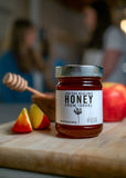 Jar of honey labeled 'Honey from Israel' on a wooden cutting board with apples and a honey dipper.