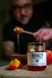 Jar of honey from Israel with a person using a honey dipper and fruit slices on a wooden surface.