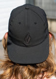 A girl wearing the a black baseball cap backwards with the UJA flame logo engraved in black.