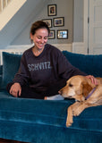 Woman in black crew neck sweatshirt with the word "SHVITZ." printed on the front. She is petting a dog.