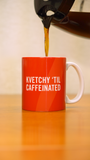 A coffee pot pouring into a burnt orange mug that says "Kvetchy 'Til Caffeinated" in white wording.