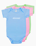Three colorful baby onesies stacked together in blue, pink, and green, all featuring the word ‘aboose!’ printed in white.