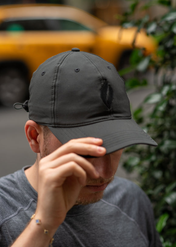 A man in NYC wearing a black baseball cap with a black UJA flame logo engraved. 