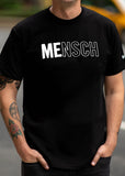 A man on the streets of NYC wearing a black shirt that says "Mensch" with the letters "Me" bolded. 