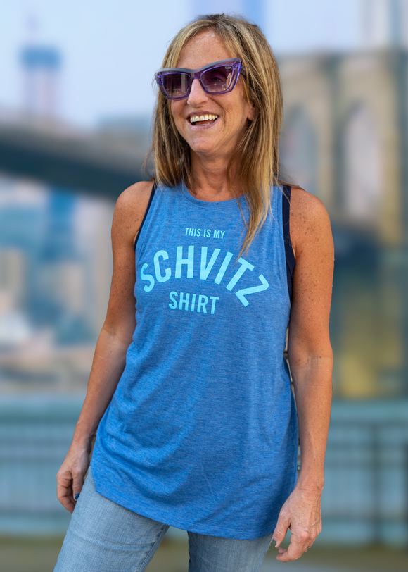 A woman standing in front of the Brooklyn Bridge wearing a blue tank top with blue letters that says "This is my SCHVITZ shirt" 