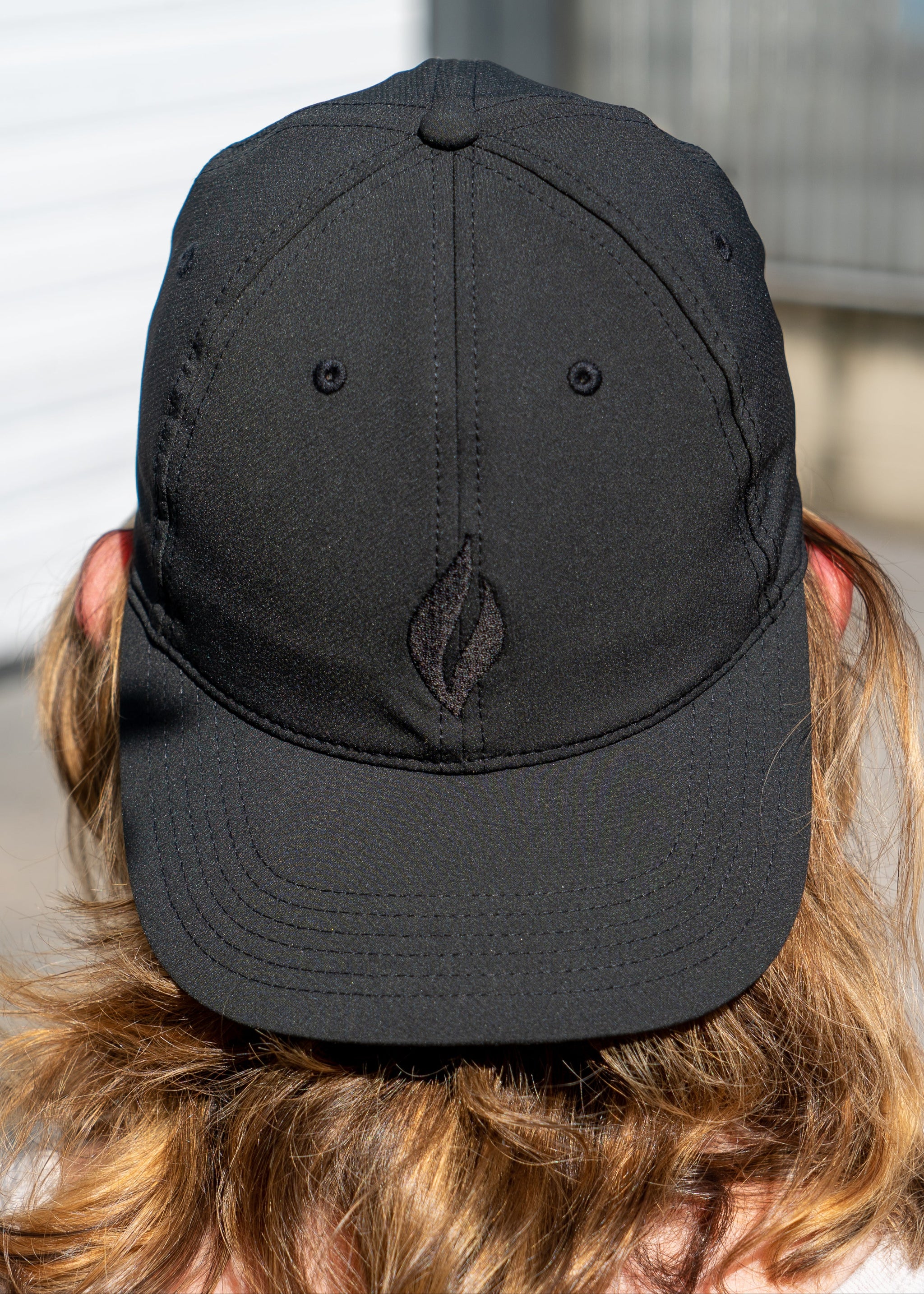 A girl wearing the a black baseball cap backwards with the UJA flame logo engraved in black. 