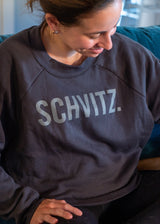 Woman in black crew neck sweatshirt with the word "SHVITZ." printed on the front. 