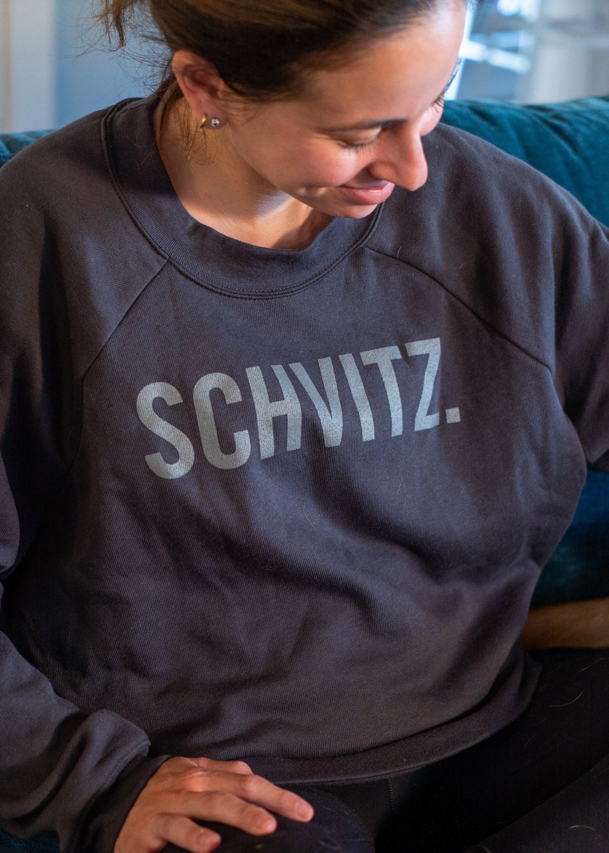 Woman in black crew neck sweatshirt with the word "SHVITZ." printed on the front. 