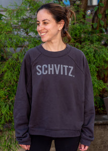 Woman in black crew neck sweatshirt with the word "SHVITZ." printed on the front. 