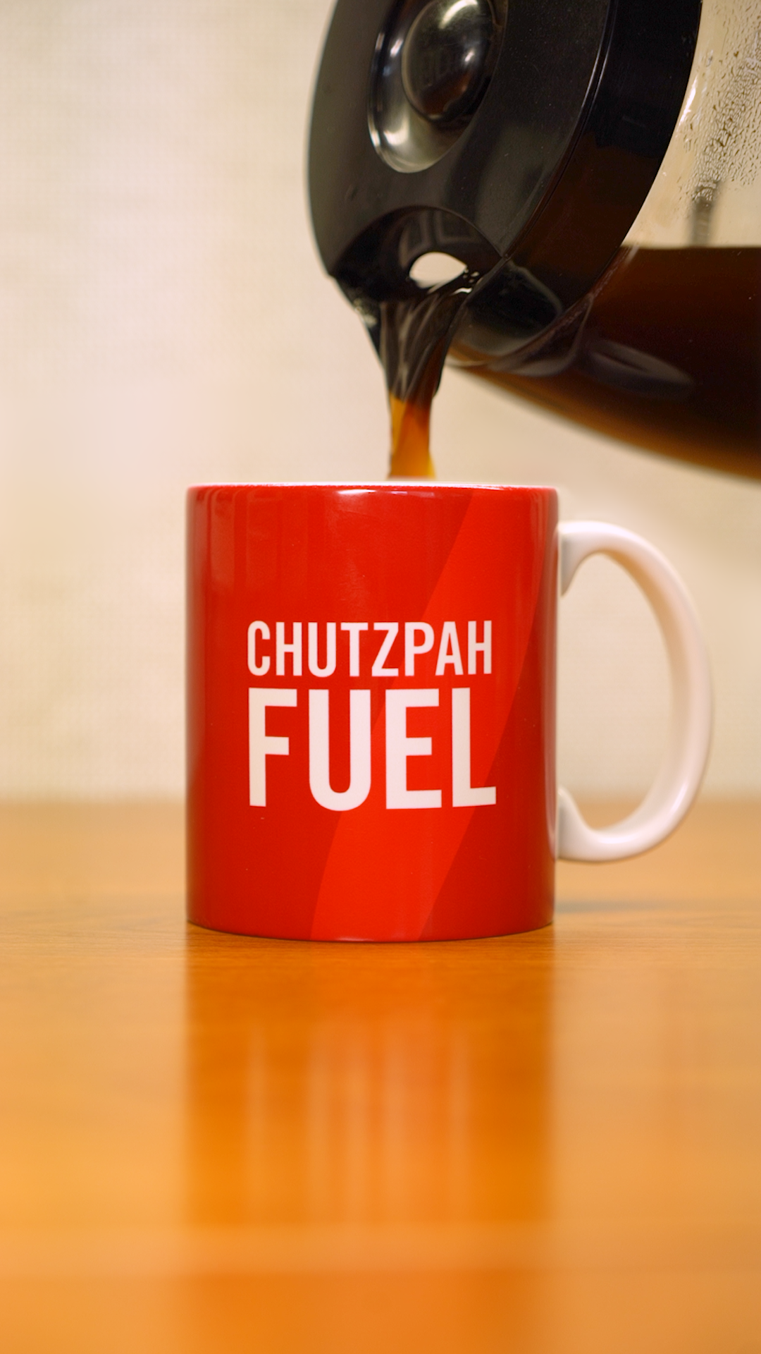 A coffee pot pouring coffee into a red mug that says "Chutzpah Fuel" in white letters. 