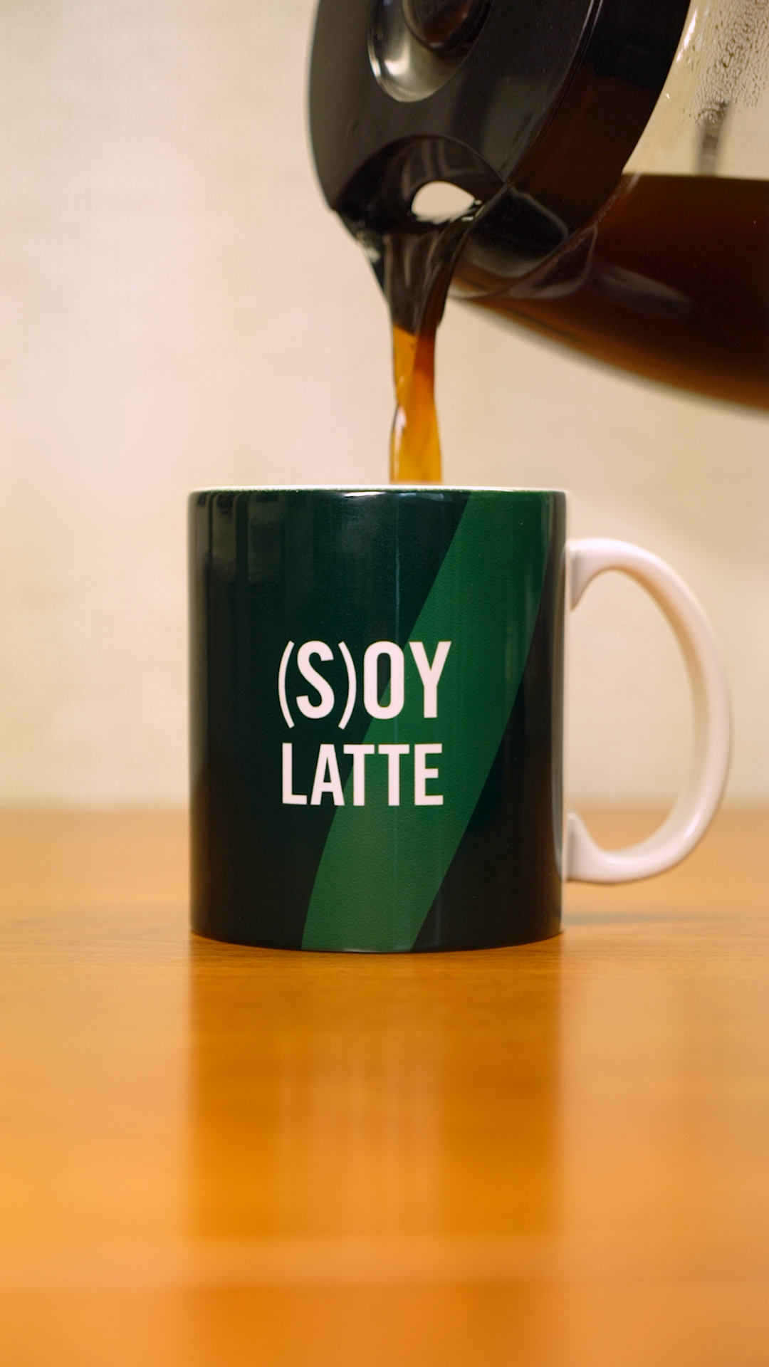 A coffee pot pouring coffee into a green mug that says "(S)oy Latte)" in white letters. 