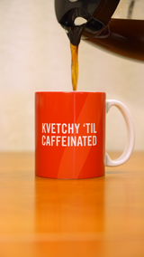 A coffee pot pouring into a burnt orange mug that says "Kvetchy 'Til Caffeinated" in white wording. 