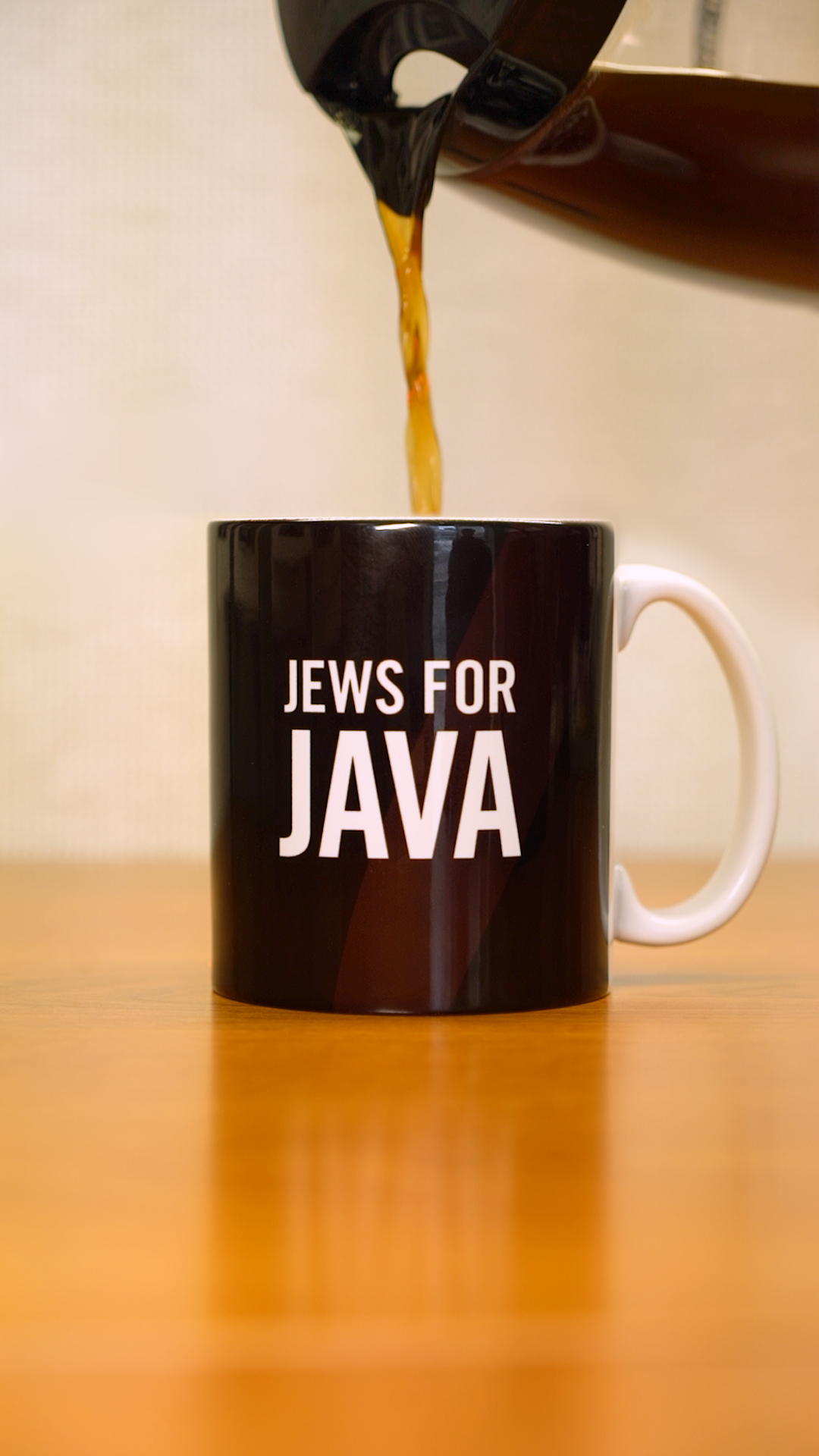 A coffee pot pouring coffee into a brown mug that says "Jews for Java" in white letters. 
