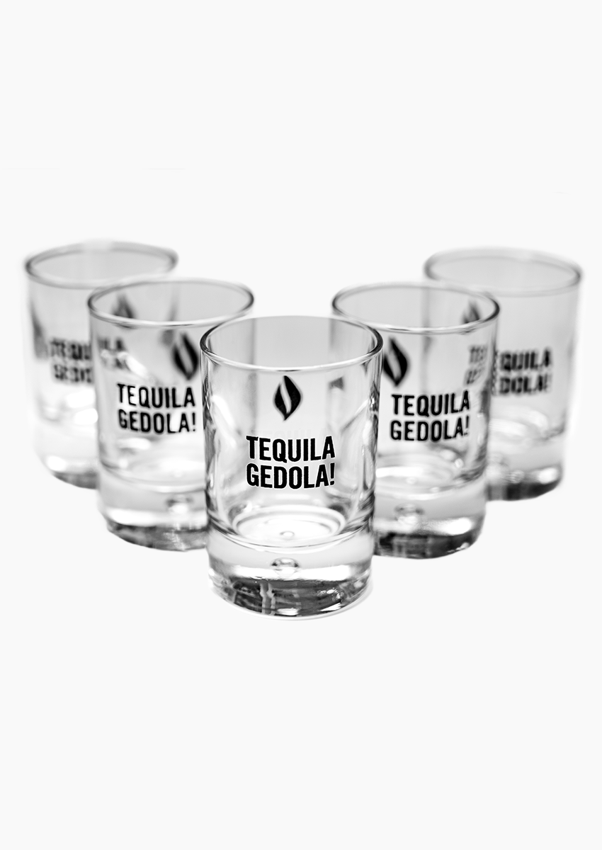 The photo features five clear shot glasses with the phrase ‘Tequila Gedola!’ and UJA flame logo printed on each glass.