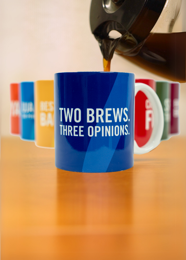 A coffee pot pouring into a blue mug that says "Two Brews. Three Opinions." in white letters. There are 6 other coffee mugs in the background with varied colors and wording. 